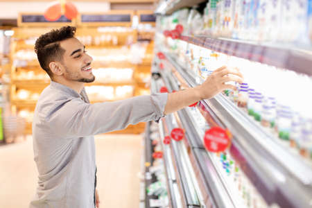 Millennial Arabic Man Shopping Groceries Choosing Dairy Products In Supermarketの写真素材