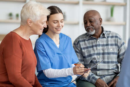 Cheerful young woman doctor having conversation with senior peopleの写真素材