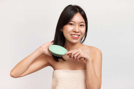 Portrait of cheerful Asian woman brushing her hairの写真素材