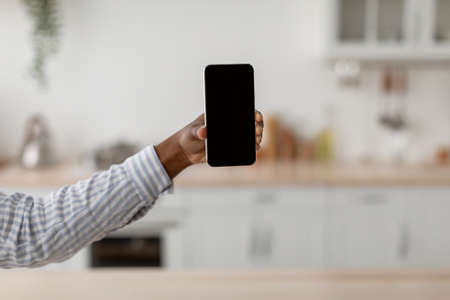 Hand of young african american woman show smartphone with blank screen at scandinavian kitchen...