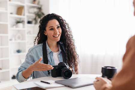 Positive Photographer Woman Talking To Lady Sitting In Modern Officeの写真素材