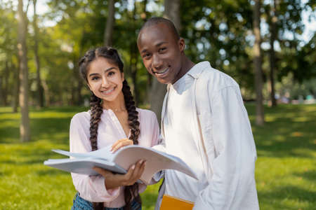 Education concept. Friendly multiracial university students preparing for exam together, holding notebook and smilingの写真素材