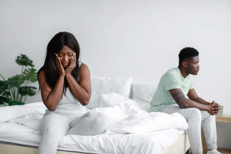 Depressed frustrated young african american wife sad and crying after quarrel, ignoring husbandの写真素材