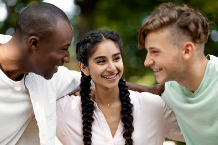 Portrait of cheerful multiracial college students walking outdoors after passing exam, embracing and sincerely laughing,の写真素材