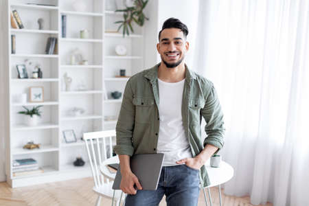 Handsome Arab Guy With Laptop In Hand Standing Near Desk At Homeの写真素材