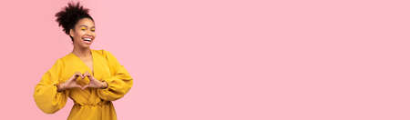 Cheerful young african american woman showing heart gesture, wide horizontal bannerの写真素材