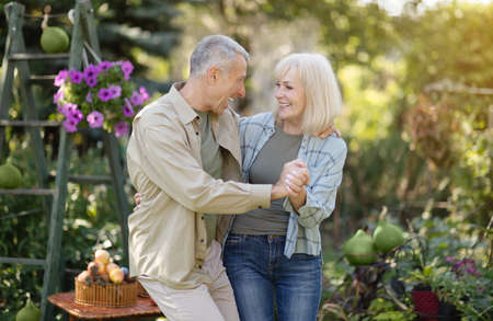 Joyful senior spouses dancing in the garden, holding hands and laughing, enjoying spending time together outdoorsの写真素材