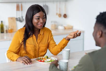 Happy Black Woman Chatting With Husband While They Having Breakfast In Kitchen