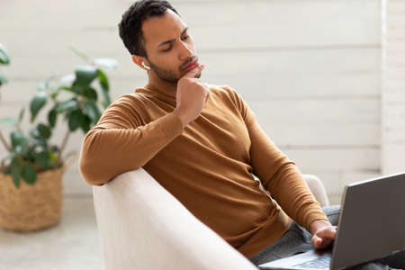 Arab man using laptop sitting on couch at home office