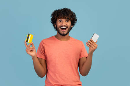 Excited hindu guy holding smartphone and credit card
