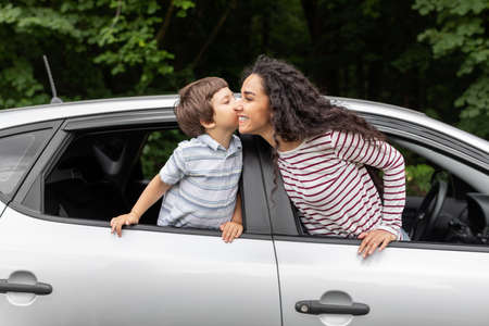Happy little boy kissing millennial mom in open car window, outdoor in summer, free spaceの写真素材
