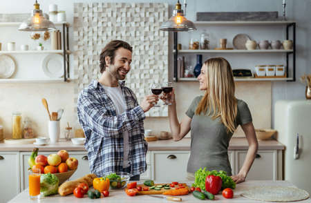 Happy millennial caucasian husband with stubble and wife cooking dinner with organic vegetablesの写真素材