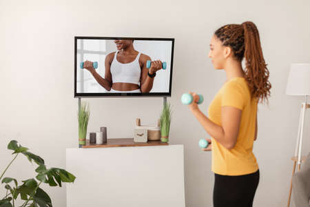 Sporty Lady Exercising Holding Dumbbells Watching Workout On Television Indoorsの写真素材