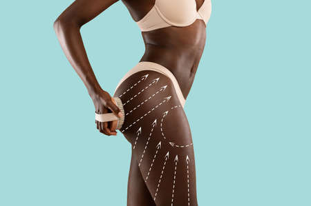 African american woman massaging hips with brush, anti cellulite treatment