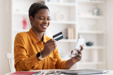 Happy african american woman using smartphone and credit card