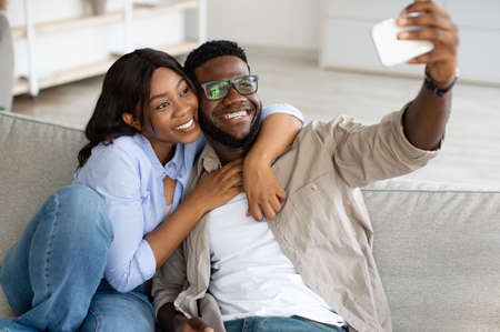 Portrait of happy black couple taking selfie together at homeの写真素材