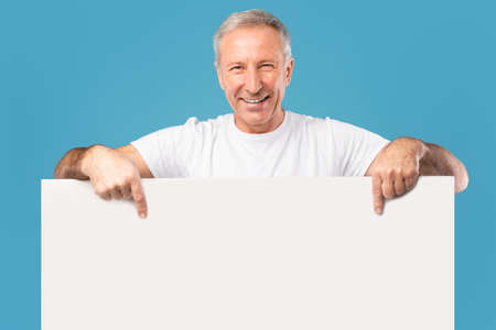 Mature man peeking out blank white advertising billboard at studio