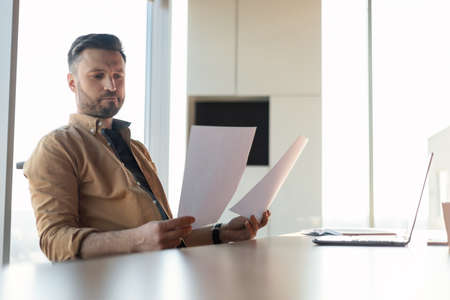 Thoughtful Businessman Reading Business Papers Holding Documents Sitting In Officeの写真素材