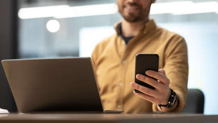 Businessman Using Smartphone Texting Using Laptop Sitting In Office, Cropped