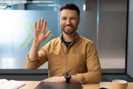 Businessman Waving Hand To Camera Having Video Call In Office