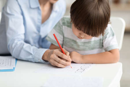 Early development training. Concentrated little boy pupil painting with teacher at kindergarten,...