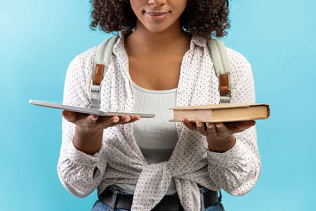 Cropped view of young black female student holding book and tablet pc, comparing offline studies and...