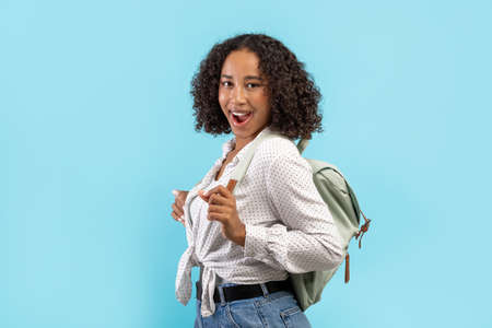 Excited African American female student with backpack shouting WOW over blue studio background