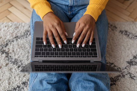 Unrecognizable young black woman sitting on floor and using laptop, working online at home, top viewの写真素材