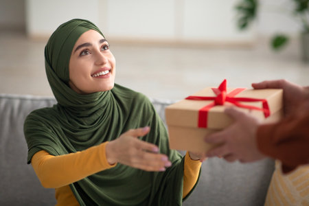 Joyful Muslim Woman Wearing Hijab Receiving Gift Box At Homeの写真素材