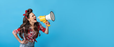 Great shopping offer. Agitated young pin up woman in retro style outfit shouting into megaphone on blue backgroundの写真素材