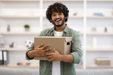 Happy young indian man hugging box at homeの写真素材