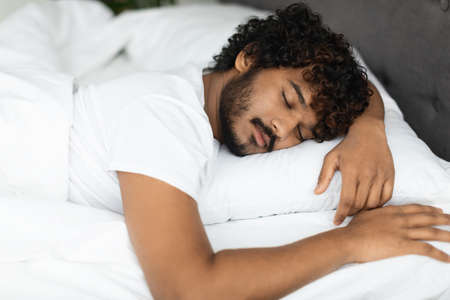 Closeup portrait of peaceful indian guy sleeping in bedの写真素材