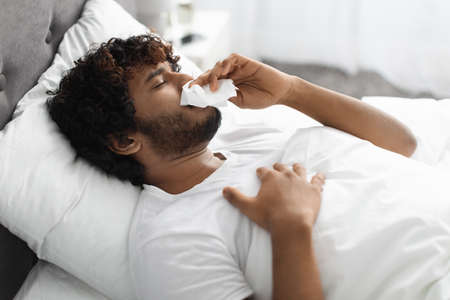 Young sick man in bed cleaning snotty noseの写真素材