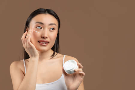 Portrait of young chinese lady with moisturizer cream on her pretty face, testing new beauty product, free spaceの写真素材