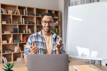Happy arab male manager sitting near empty whiteboard and explaining new business strategy to...