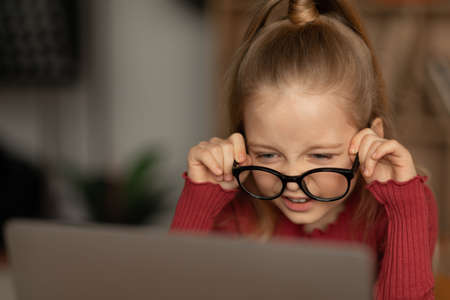 Little Girl With Poor Eyesight Wearing Eyeglasses Using Laptop Indoorsの写真素材