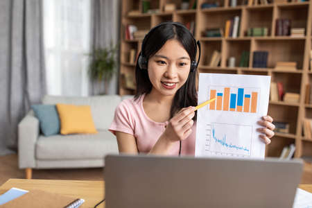 Young korean financial analyst having video call on laptop, giving virtual presentation and showing...