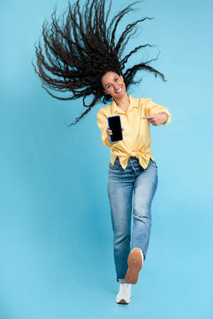 Cheerful lady jumping and pointing at empty smart phone screen
