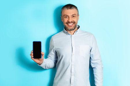 Cheerful Middle Aged Man Holding Smartphone Showing Screen, Blue Background