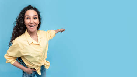 Excited woman pointing finger back at copy space