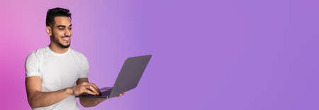 Smiling young Arab man working on laptop, having video call, chatting online in neon light, banner...