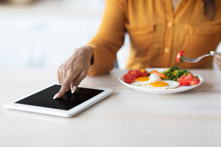 Cropped of black lady using digital tablet during breakfastの写真素材