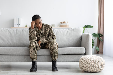 Upset Pensive Black Military Woman In Uniform Sitting On Couch At Homeの写真素材