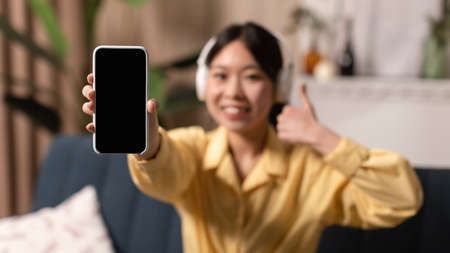 Smiling Asian woman showing blank phone screen and like, mockupの写真素材