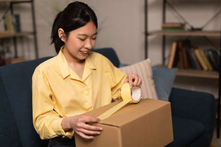Happy Asian woman packing parcel using duct tapeの写真素材