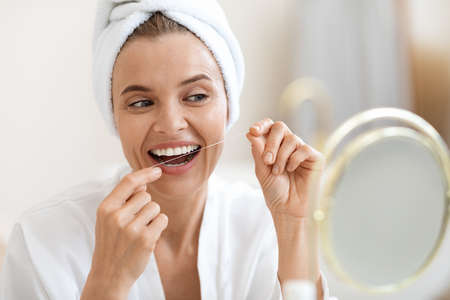 Adult woman using dental floss, cleaning her beautiful white teeth