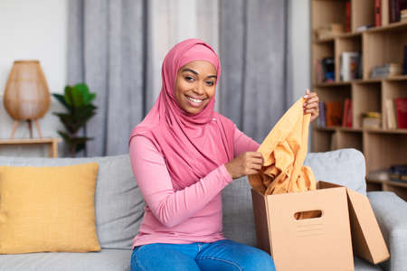 Delivery and online shopping. Happy african american lady holding piece of clothes, unpacking cardboard boxの写真素材