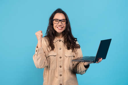 Happy young european female brunette student in glasses rejoices to victory and success deal, hold...