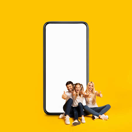 Joyful Family Sitting Near Big Blank Smartphone And Showing Thumbs Upの写真素材