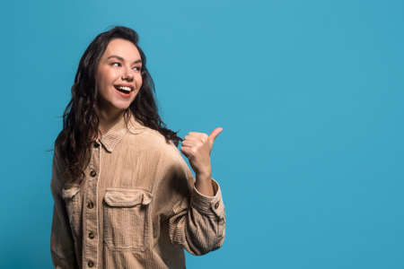 Satisfied millennial european brunette female in casual with open mouth points finger at copy spaceの写真素材